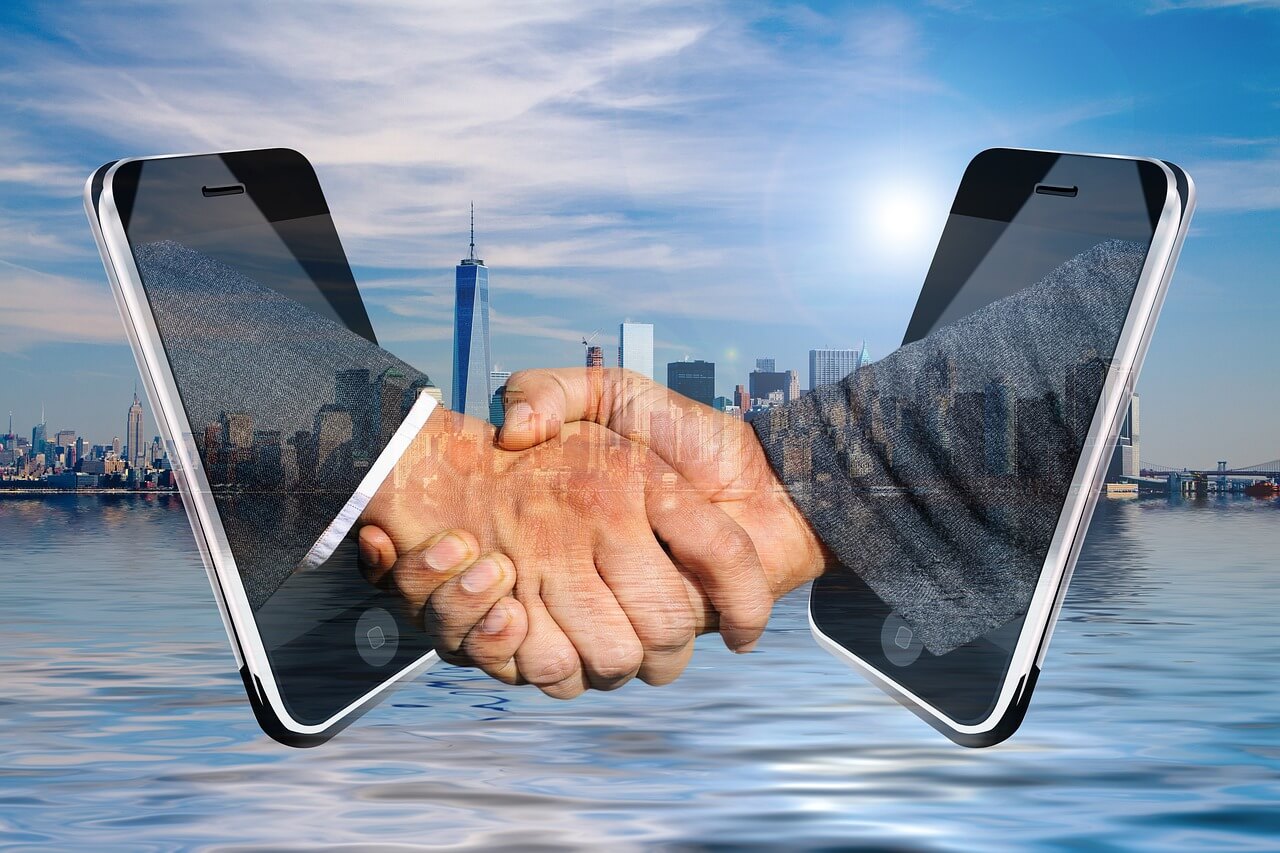 Hands shaking through mobile phones symbolizing an online agreement